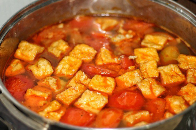Cho tất cả cà chua xào vào nồi nước dùng đang ninh sôi cùng với phần đậu phụ đã chiên.